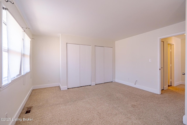 unfurnished bedroom featuring light carpet, baseboards, visible vents, and multiple closets