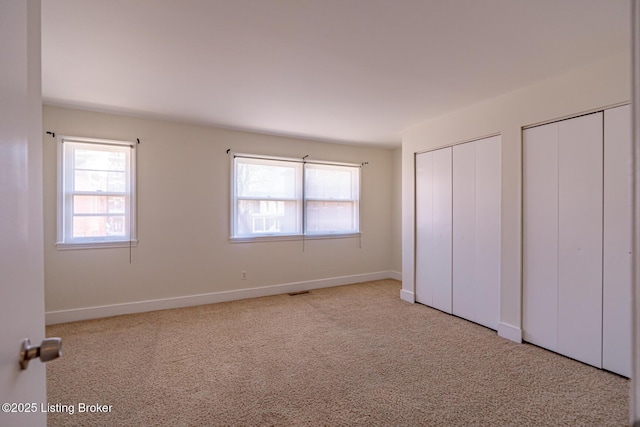 unfurnished bedroom featuring carpet, multiple windows, baseboards, and multiple closets