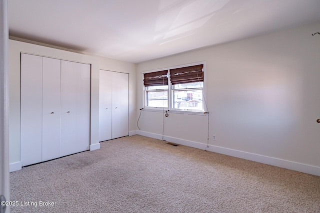 unfurnished bedroom featuring carpet floors, baseboards, visible vents, and multiple closets