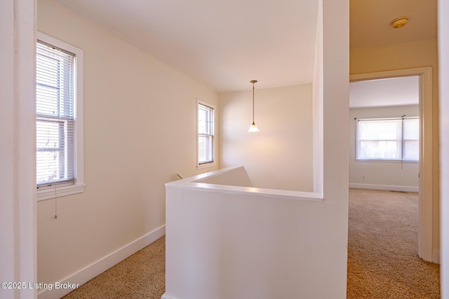 hall with carpet, baseboards, and an upstairs landing