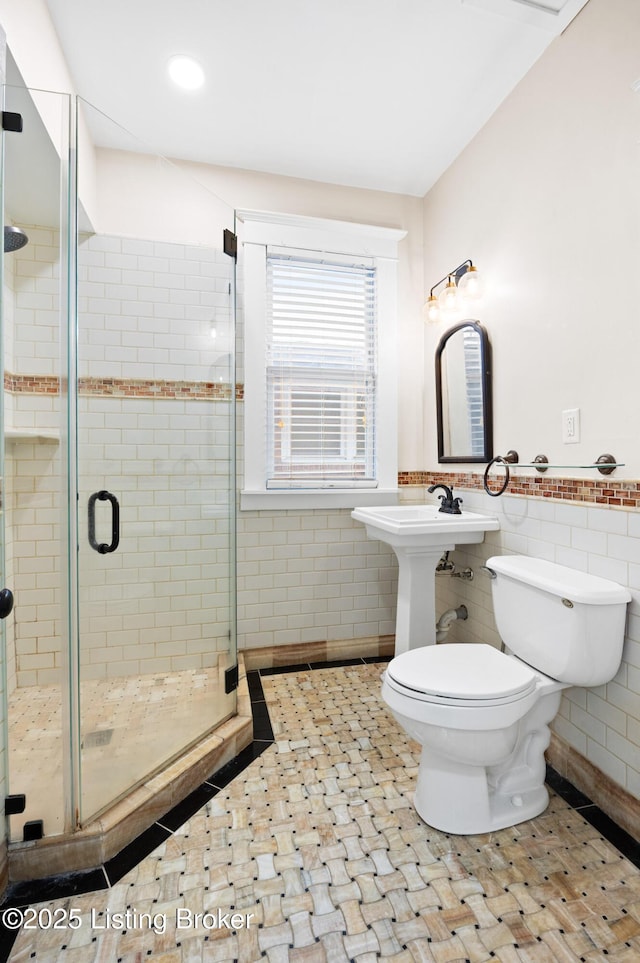 bathroom with toilet, sink, tile walls, and a shower with shower door