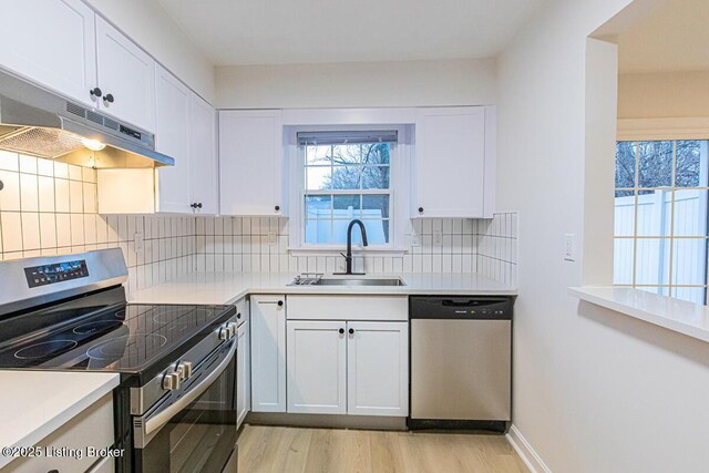 kitchen with appliances with stainless steel finishes, tasteful backsplash, sink, white cabinets, and light hardwood / wood-style flooring