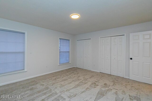 unfurnished bedroom featuring multiple closets and light colored carpet