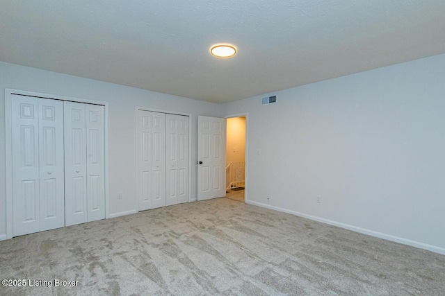 unfurnished bedroom with light carpet and two closets