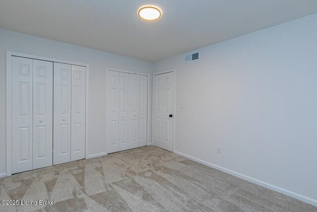 unfurnished bedroom featuring multiple closets and light colored carpet