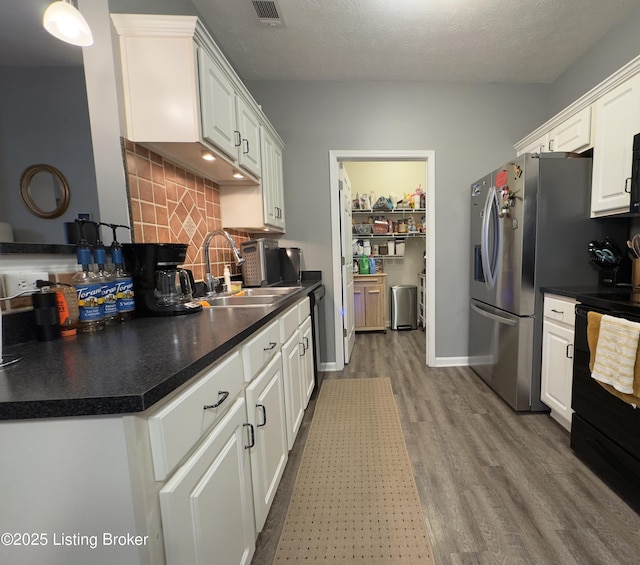 kitchen with sink, black range oven, light hardwood / wood-style flooring, decorative backsplash, and white cabinets