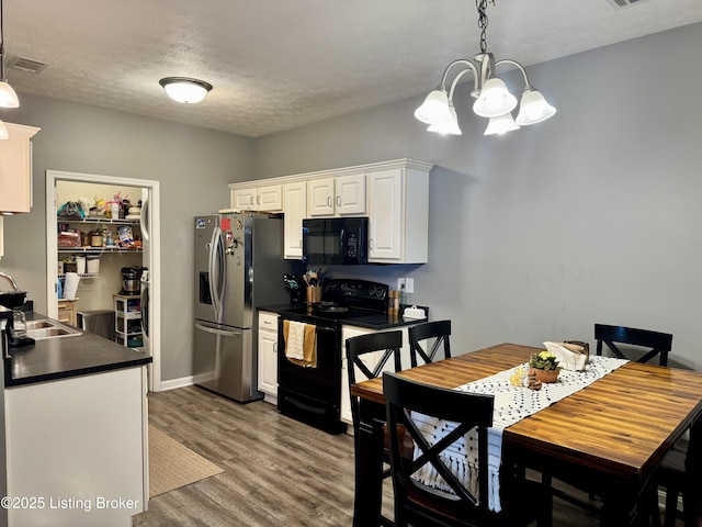 kitchen featuring dark wood-type flooring, sink, black appliances, hanging light fixtures, and white cabinets