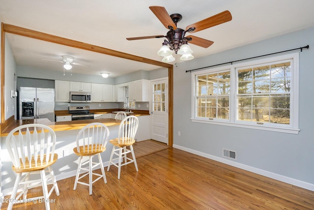 kitchen with white cabinetry, sink, kitchen peninsula, stainless steel appliances, and light wood-type flooring