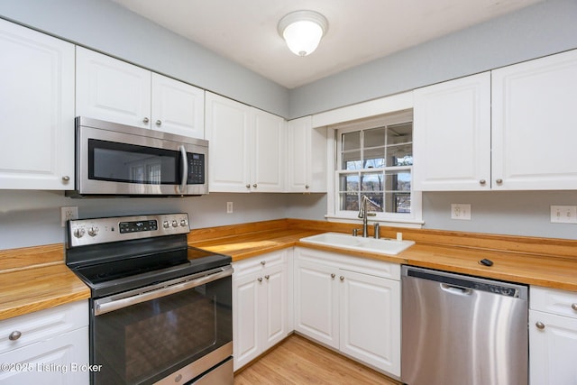 kitchen with appliances with stainless steel finishes, wood counters, sink, white cabinets, and light wood-type flooring