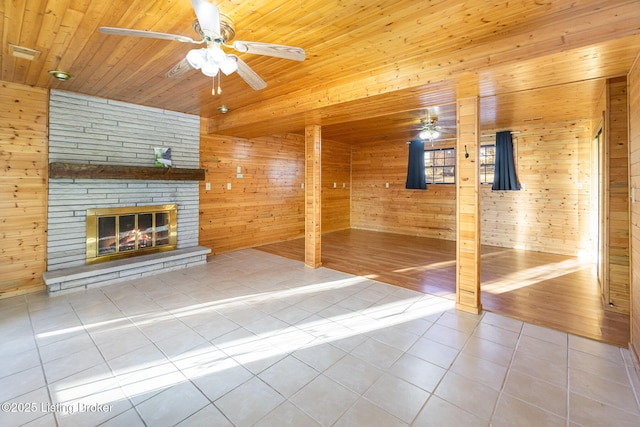 unfurnished living room featuring ceiling fan, wooden ceiling, tile patterned floors, and wooden walls