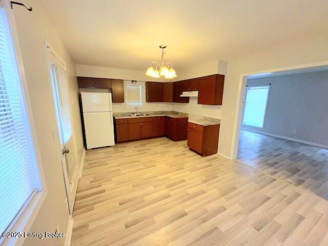 kitchen with a chandelier, hanging light fixtures, white fridge, and light hardwood / wood-style flooring