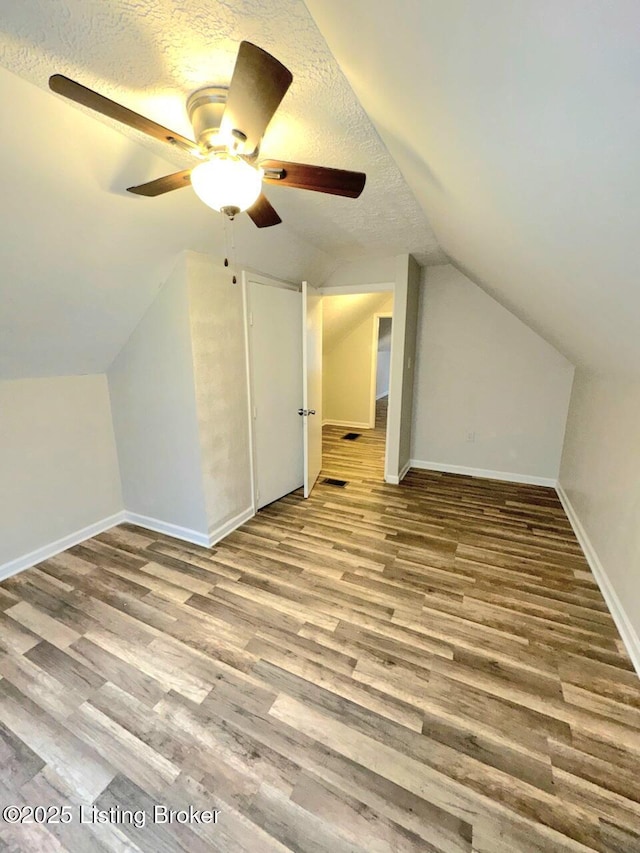 bonus room with ceiling fan, hardwood / wood-style flooring, vaulted ceiling, and a textured ceiling