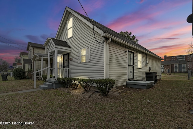 property exterior at dusk featuring cooling unit and a lawn