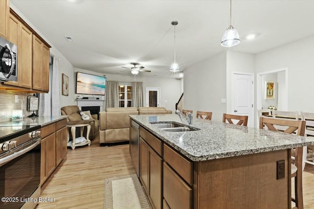 kitchen with sink, appliances with stainless steel finishes, hanging light fixtures, a kitchen breakfast bar, and light stone counters