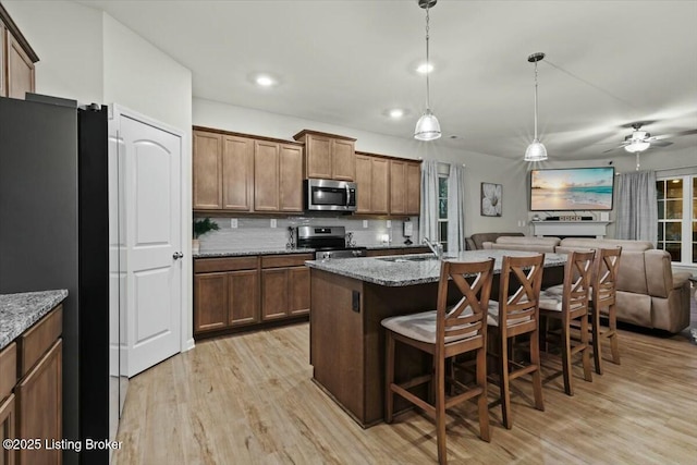 kitchen with decorative light fixtures, a kitchen breakfast bar, stainless steel appliances, light stone countertops, and a center island with sink