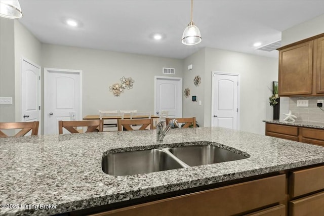 kitchen featuring hanging light fixtures, tasteful backsplash, light stone countertops, and sink