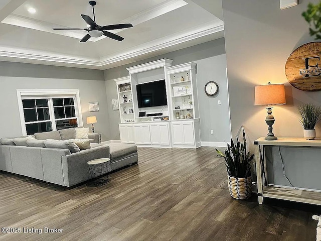 living room featuring dark wood-type flooring, ceiling fan, ornamental molding, and a tray ceiling