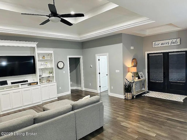 living room with dark wood-type flooring, ceiling fan, ornamental molding, and a tray ceiling