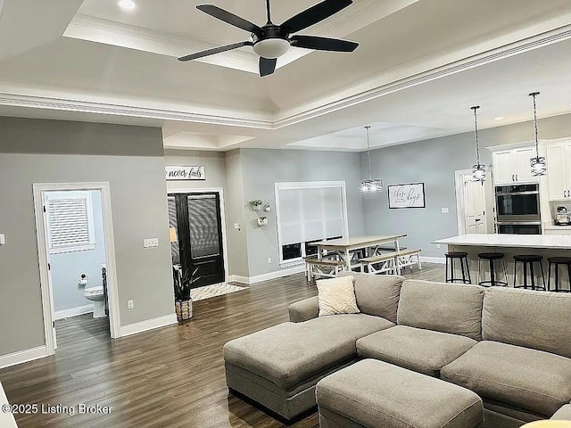 living room featuring dark hardwood / wood-style flooring, ornamental molding, a raised ceiling, and ceiling fan