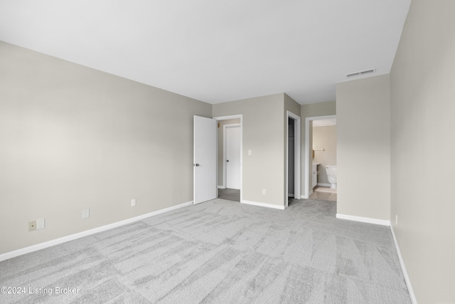 unfurnished bedroom featuring light colored carpet and ensuite bathroom