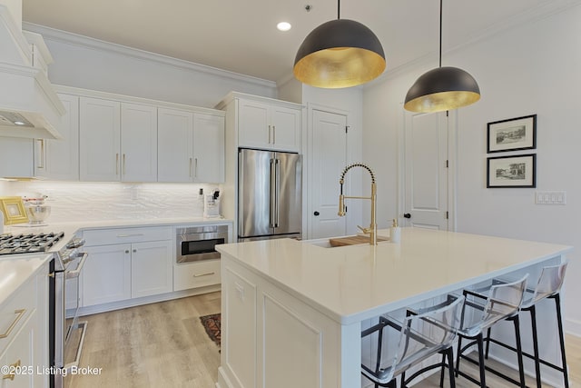 kitchen with custom exhaust hood, hanging light fixtures, an island with sink, stainless steel appliances, and white cabinets