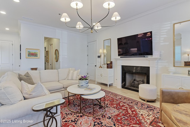 living room featuring a notable chandelier, ornamental molding, a fireplace, and light hardwood / wood-style floors