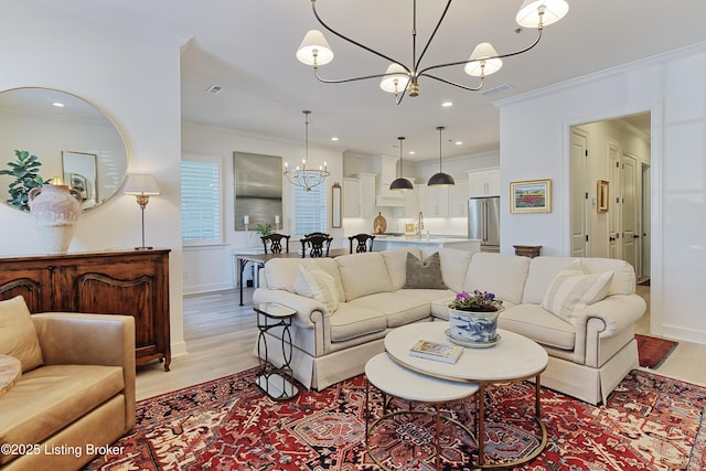 living room with an inviting chandelier, ornamental molding, sink, and light hardwood / wood-style flooring