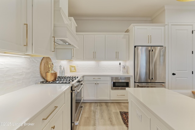 kitchen featuring premium range hood, stainless steel appliances, crown molding, and white cabinets