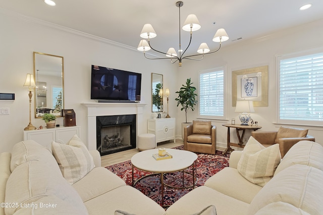 living room with a notable chandelier, a fireplace, ornamental molding, and light wood-type flooring