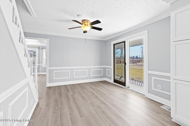 empty room featuring a textured ceiling, ornamental molding, light hardwood / wood-style floors, and ceiling fan