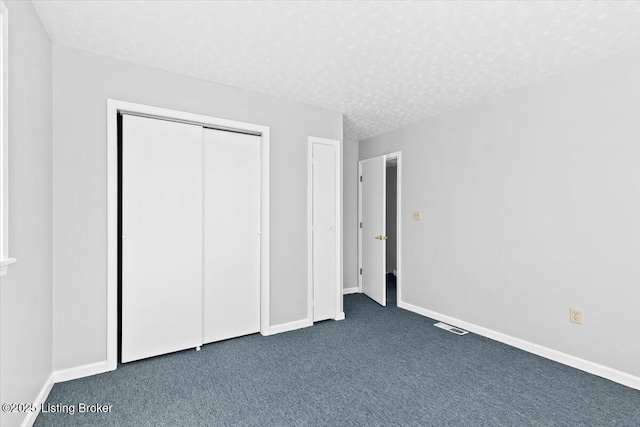 unfurnished bedroom featuring a closet, a textured ceiling, and dark colored carpet