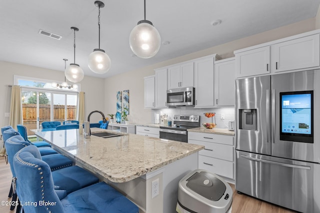 kitchen featuring sink, stainless steel appliances, white cabinets, a center island with sink, and decorative light fixtures