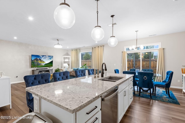 kitchen featuring sink, dishwasher, hanging light fixtures, white cabinets, and a center island with sink