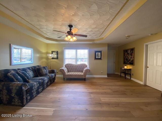 living room with ceiling fan, wood-type flooring, and a tray ceiling