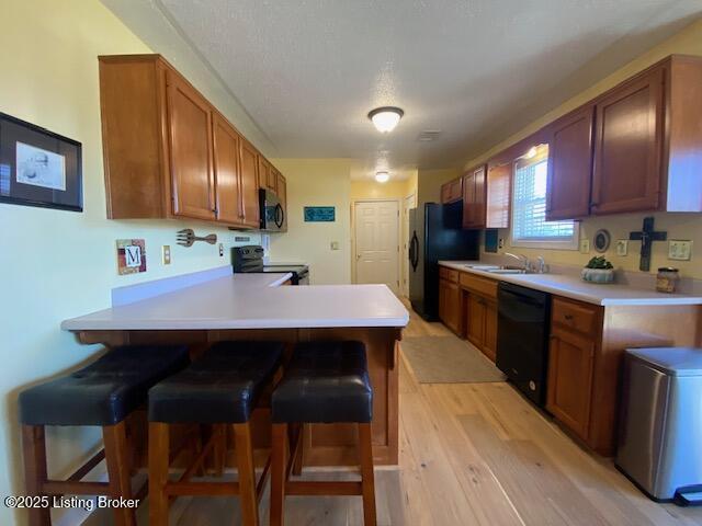 kitchen featuring black appliances, sink, a kitchen bar, kitchen peninsula, and light wood-type flooring