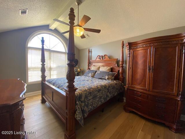 bedroom featuring ceiling fan, light hardwood / wood-style floors, a textured ceiling, and vaulted ceiling with beams