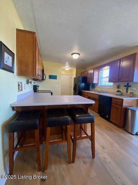 kitchen with a breakfast bar, light hardwood / wood-style floors, kitchen peninsula, and black appliances