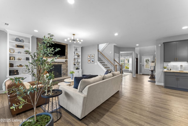 living room featuring an inviting chandelier, hardwood / wood-style flooring, a stone fireplace, and built in features