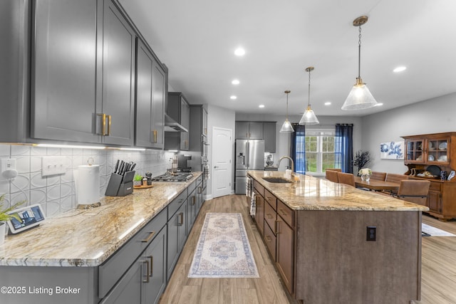 kitchen with a large island, sink, hanging light fixtures, stainless steel appliances, and light stone counters