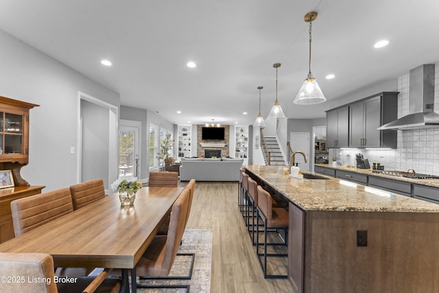 kitchen featuring sink, a breakfast bar area, a large fireplace, stainless steel gas cooktop, and wall chimney exhaust hood