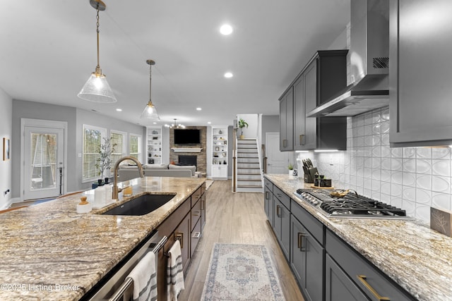 kitchen with decorative light fixtures, sink, light stone counters, stainless steel appliances, and wall chimney range hood