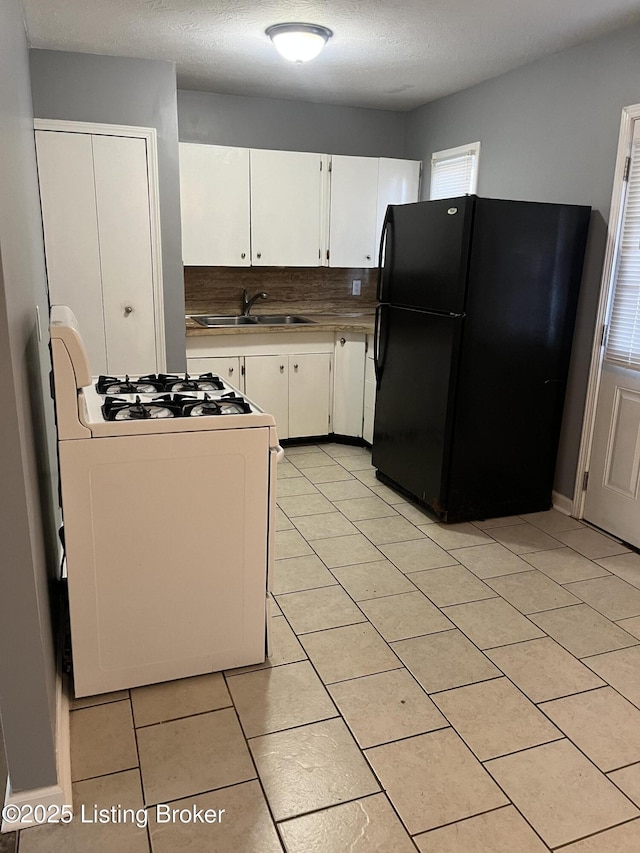 kitchen featuring black fridge, white gas range, sink, and white cabinets