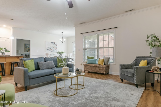 living room with ornamental molding, ceiling fan with notable chandelier, and light hardwood / wood-style floors