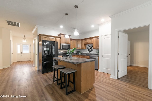 kitchen with appliances with stainless steel finishes, hardwood / wood-style floors, a kitchen breakfast bar, ornamental molding, and a kitchen island