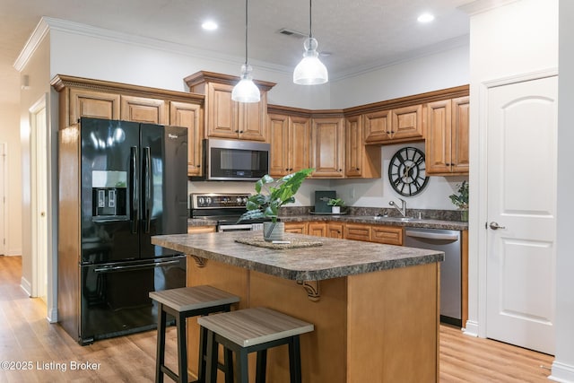 kitchen with a center island, hanging light fixtures, light wood-type flooring, ornamental molding, and stainless steel appliances