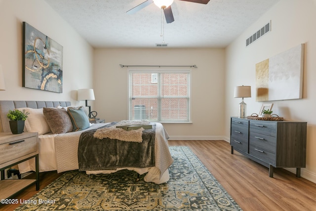 bedroom with ceiling fan, a textured ceiling, and light hardwood / wood-style floors