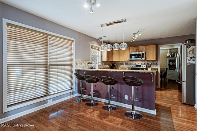 kitchen featuring appliances with stainless steel finishes, decorative light fixtures, backsplash, kitchen peninsula, and light stone countertops