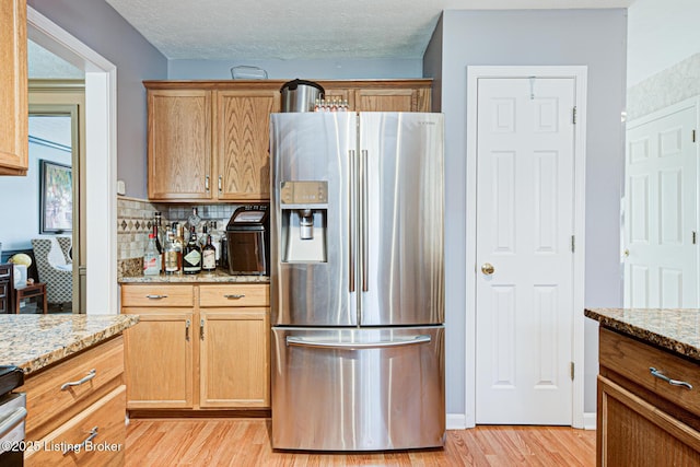 kitchen with light wood-type flooring, light stone countertops, a textured ceiling, and stainless steel refrigerator with ice dispenser