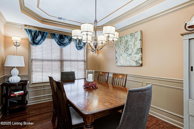 dining area featuring dark wood-type flooring, ornamental molding, a raised ceiling, and a chandelier