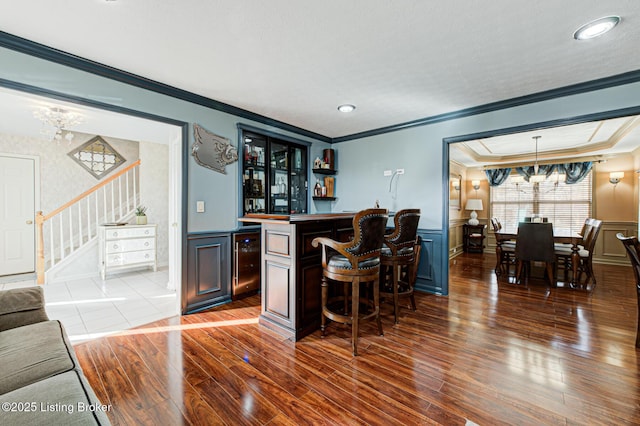 bar featuring decorative light fixtures, wine cooler, hardwood / wood-style flooring, ornamental molding, and a notable chandelier